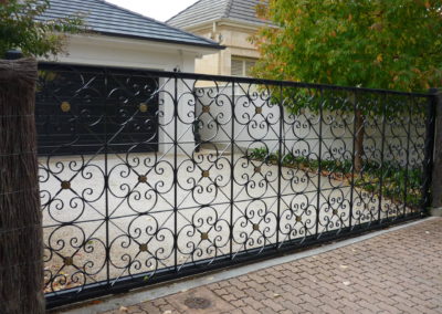 Automated electric, slide opening  single driveway gate, highly decorative panels painted black.